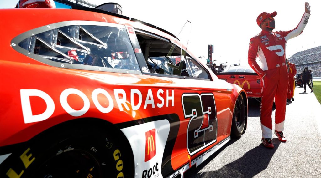 Bubba Wallace waving to fans in front of #23 Doordash Toyota